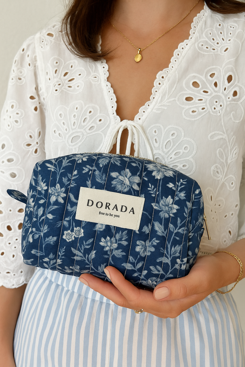 Person holding a blue floral-patterned pouch with 'DORADA' branding.